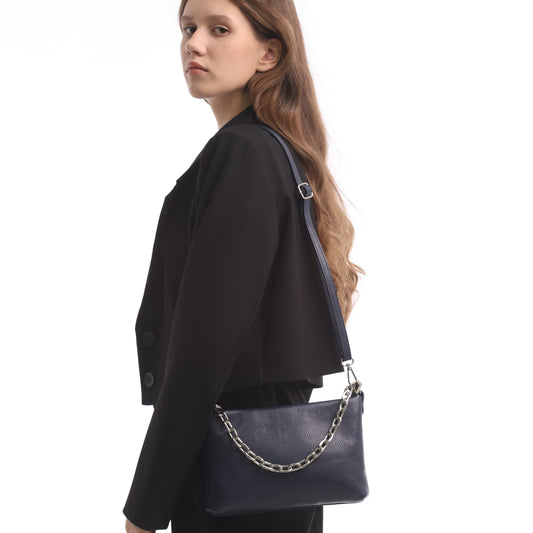 Woman in black wearing the navy Tony Perotti Borsa CA045-01BL bag on its long leather strap over one shoulder, the chain handle lying across the front