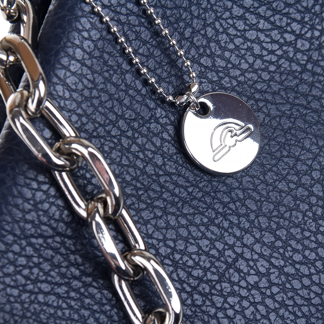 Close-up of the silver chain handle and the ball-chain zip pull with a round Tony Perotti disc charm against the navy pebbled leather
