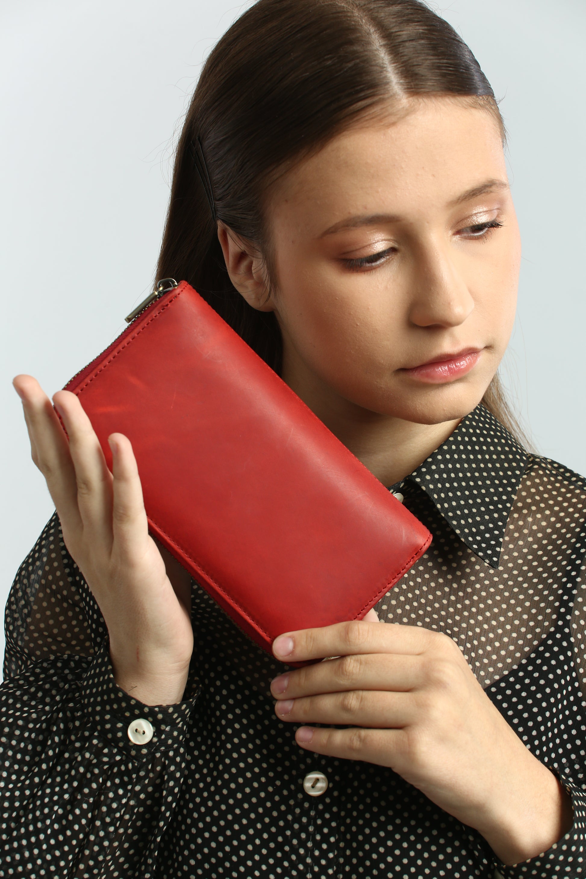 Woman holding a Tony Perotti red vintage-look leather wallet against a light gray background