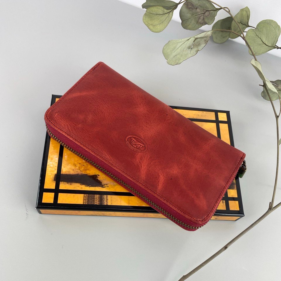 Tony Perotti red vintage-look leather zip-around wallet on a box with a plant in the background