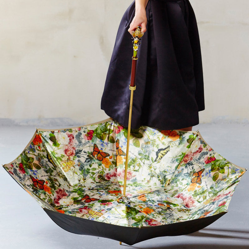 Person holding a floral and butterfly-patterned umbrella against a neutral background