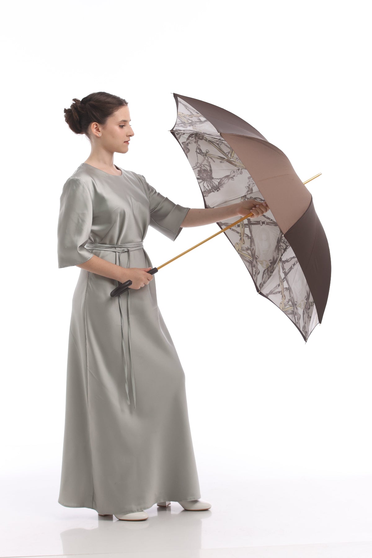 Woman in a long silver dress holding a patterned umbrella on a white background