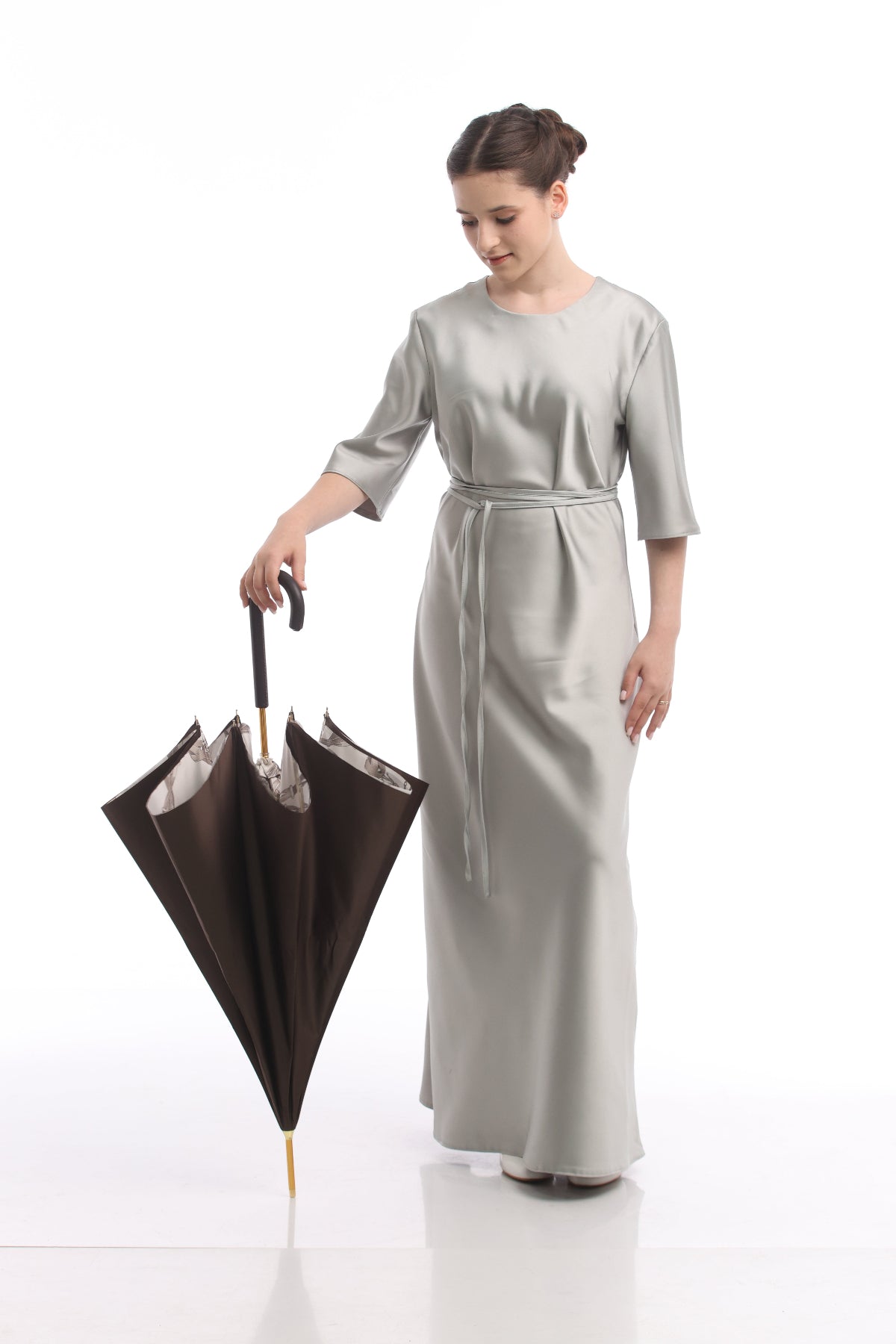 Woman in a long light gray dress holding a black umbrella on a white background