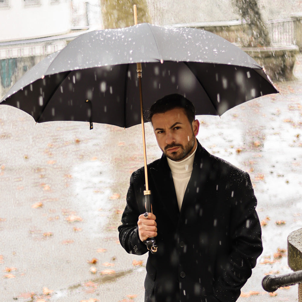 Man in a black coat under the open black Pasotti umbrella with panther handle in falling snow