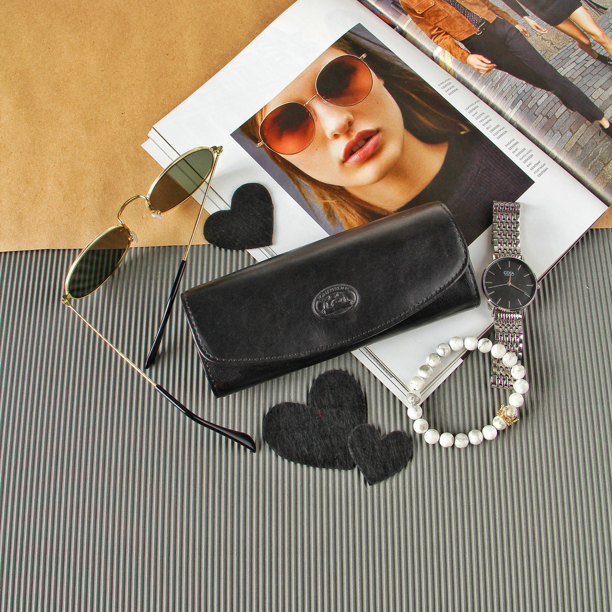 Black leather glasses case Tony Perotti Italico 1290 nero styled with round sunglasses, a watch and a magazine