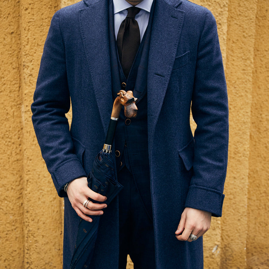 Man in a navy coat holding the furled umbrella by its schnauzer handle