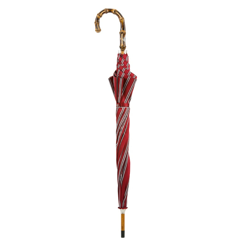 Closed red striped umbrella standing upright with bamboo crook handle