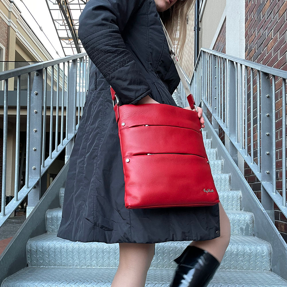 Woman in a black coat on a metal staircase carrying the red Tony Perotti Contatto 9579-28 rosso leather bag across the body