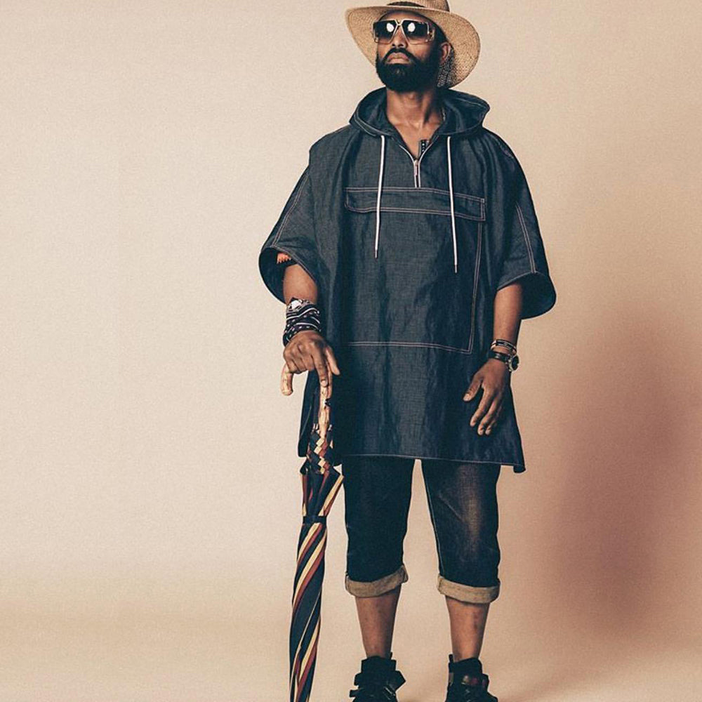 Man in a denim poncho and straw hat leaning on the furled striped umbrella