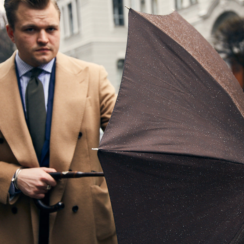 Man in a camel coat opening the brown umbrella