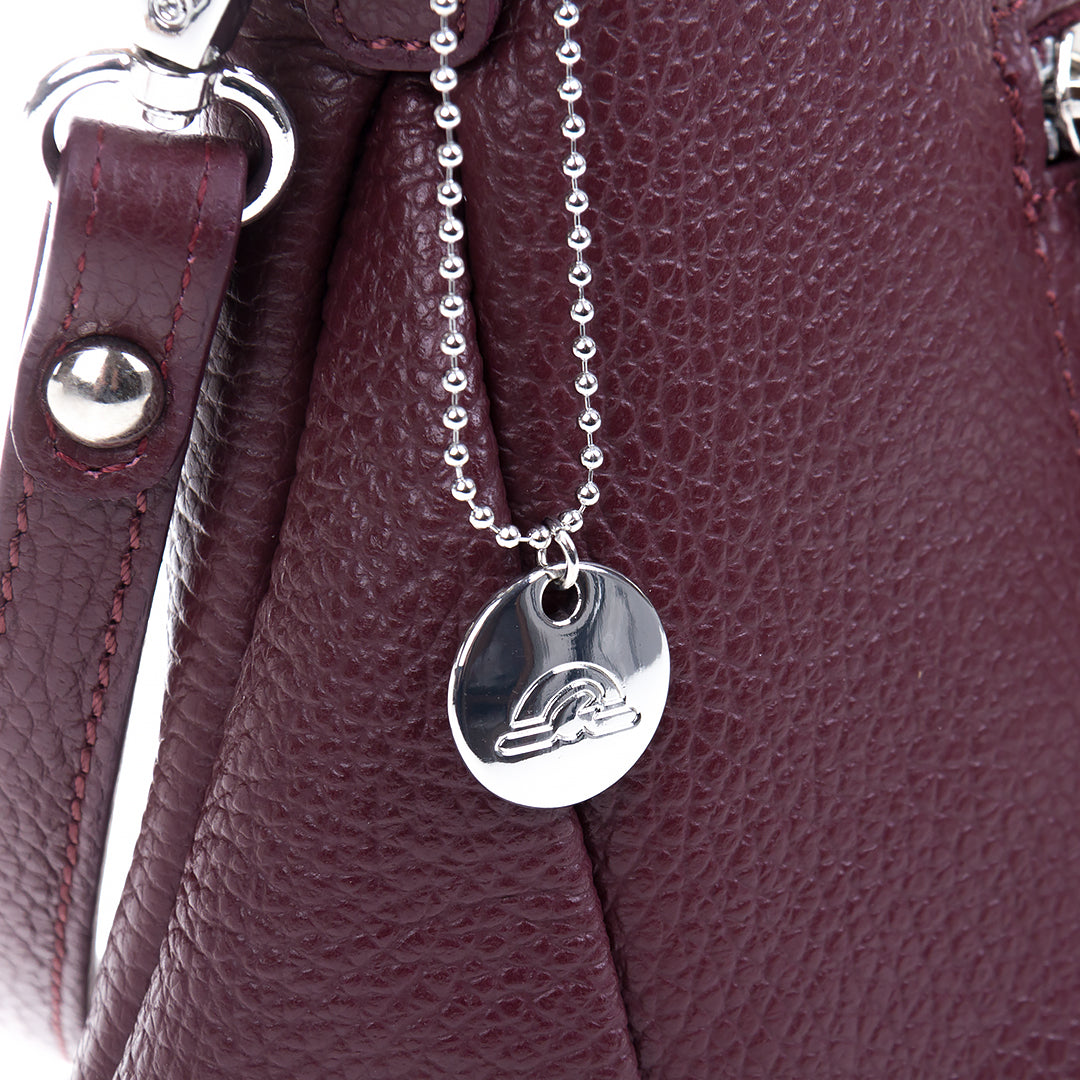 Close-up of the ball-chain zip pull with a round Tony Perotti disc charm against the burgundy pebbled leather