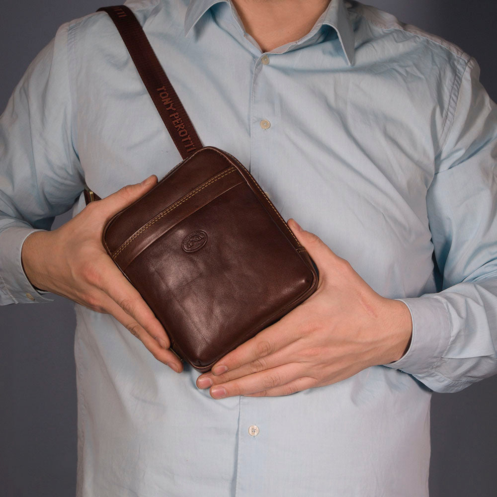 Man holding the small dark brown Tony Perotti Italico 6056 crossbody bag worn on the branded strap