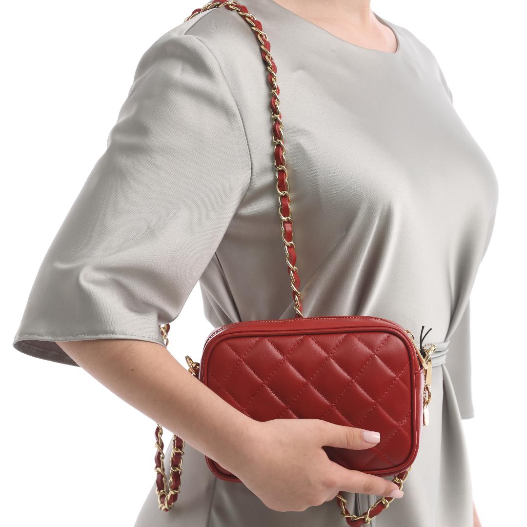 Woman in a grey dress wearing the red quilted Tony Perotti Borsa CA006-01DR bag on its chain strap at hip height, showing how small the bag is